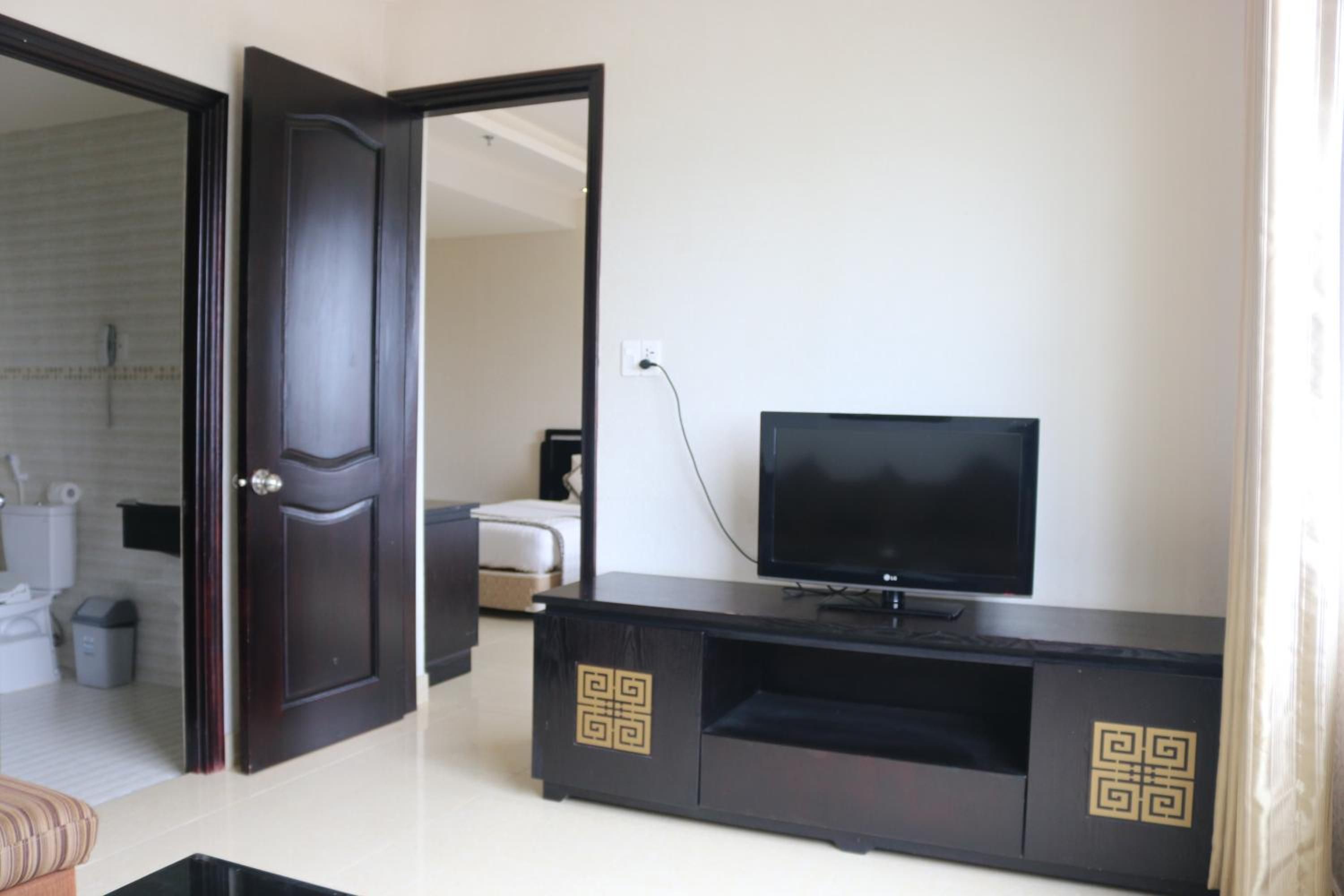 Habitación de hotel con una unidad de entretenimiento de madera oscura, un televisor y una puerta que da a un baño.