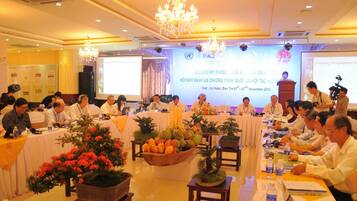 A conference room with a long table set for a meeting, a podium, and a screen displaying a presentation.