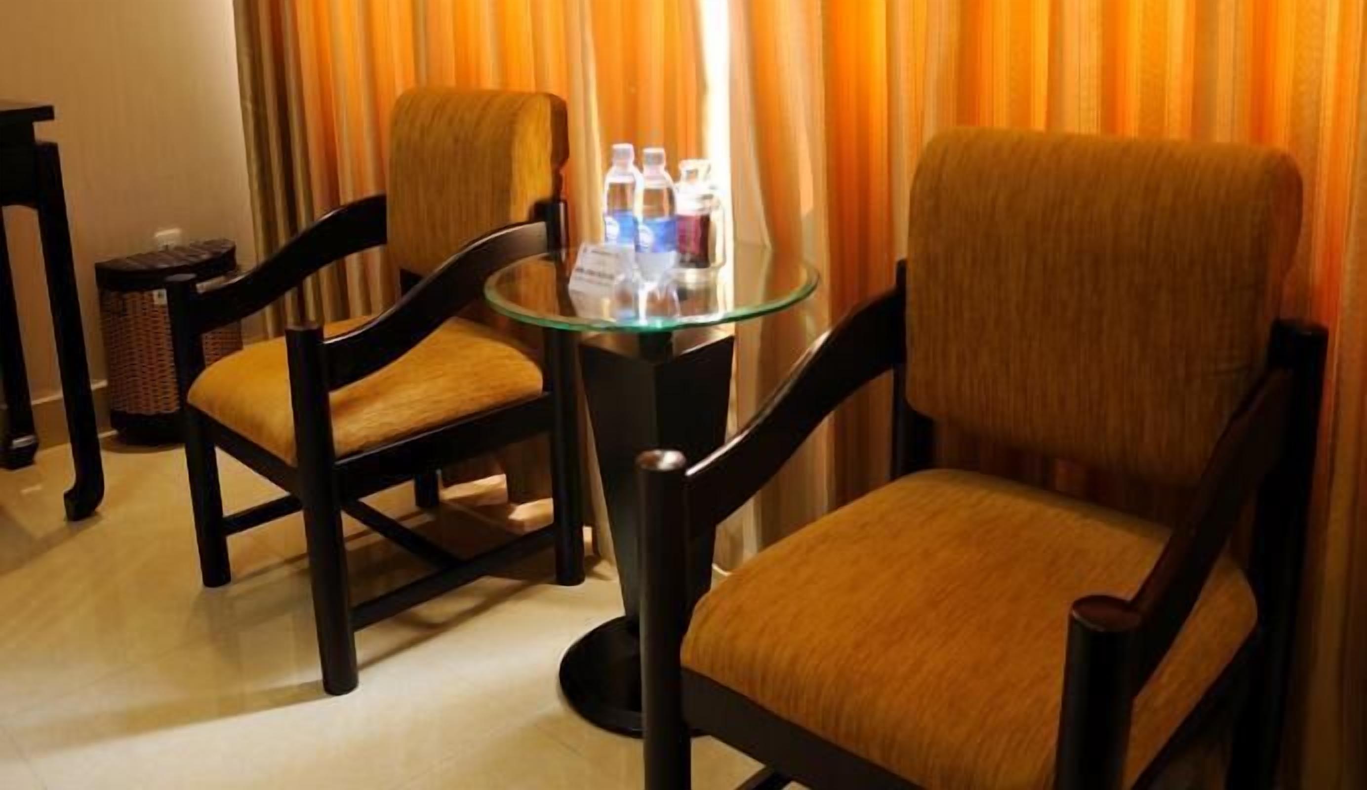 Quarto de hotel com duas cadeiras de madeira e uma mesa de vidro com garrafas de água.