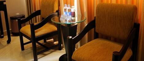 Une chambre d’hôtel avec deux chaises en bois et une table en verre sur laquelle se trouvent des bouteilles d’eau.