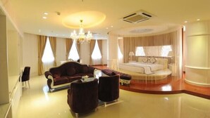 A spacious hotel room with a large bed, a sitting area with a sofa and armchairs, a chandelier, and large windows with curtains. - Viet Uc Hotel (An Hoi)