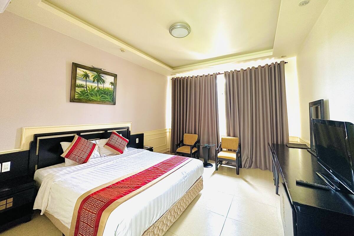 Una habitación de hotel con cama, dos sillones, escritorio y televisor.