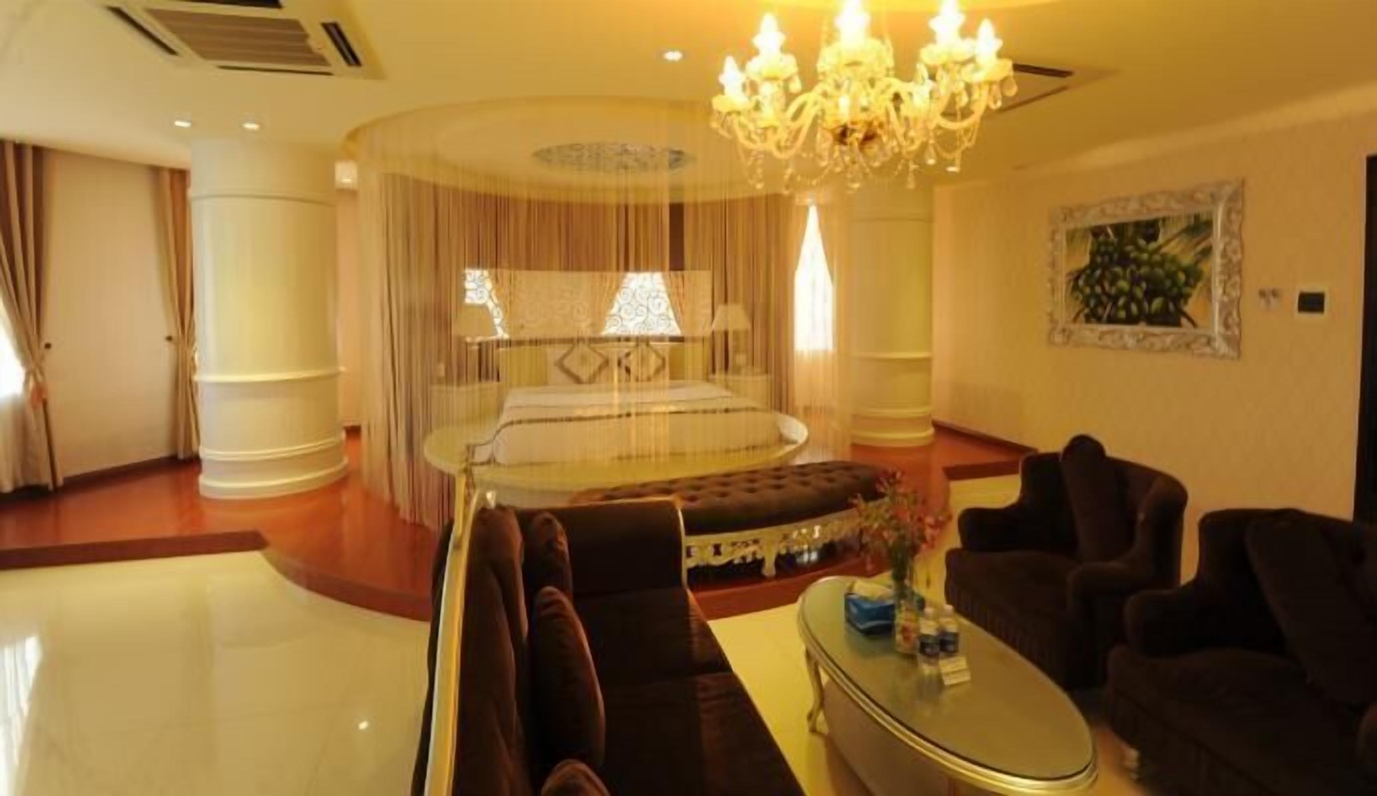 A luxurious bedroom with a large bed, a sitting area with sofas, a chandelier, and a painting on the wall.