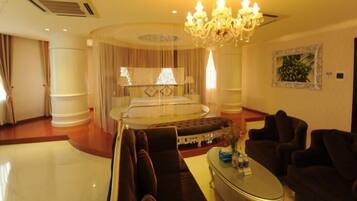 A luxurious bedroom with a large bed, a sitting area with sofas, a chandelier, and a painting on the wall.