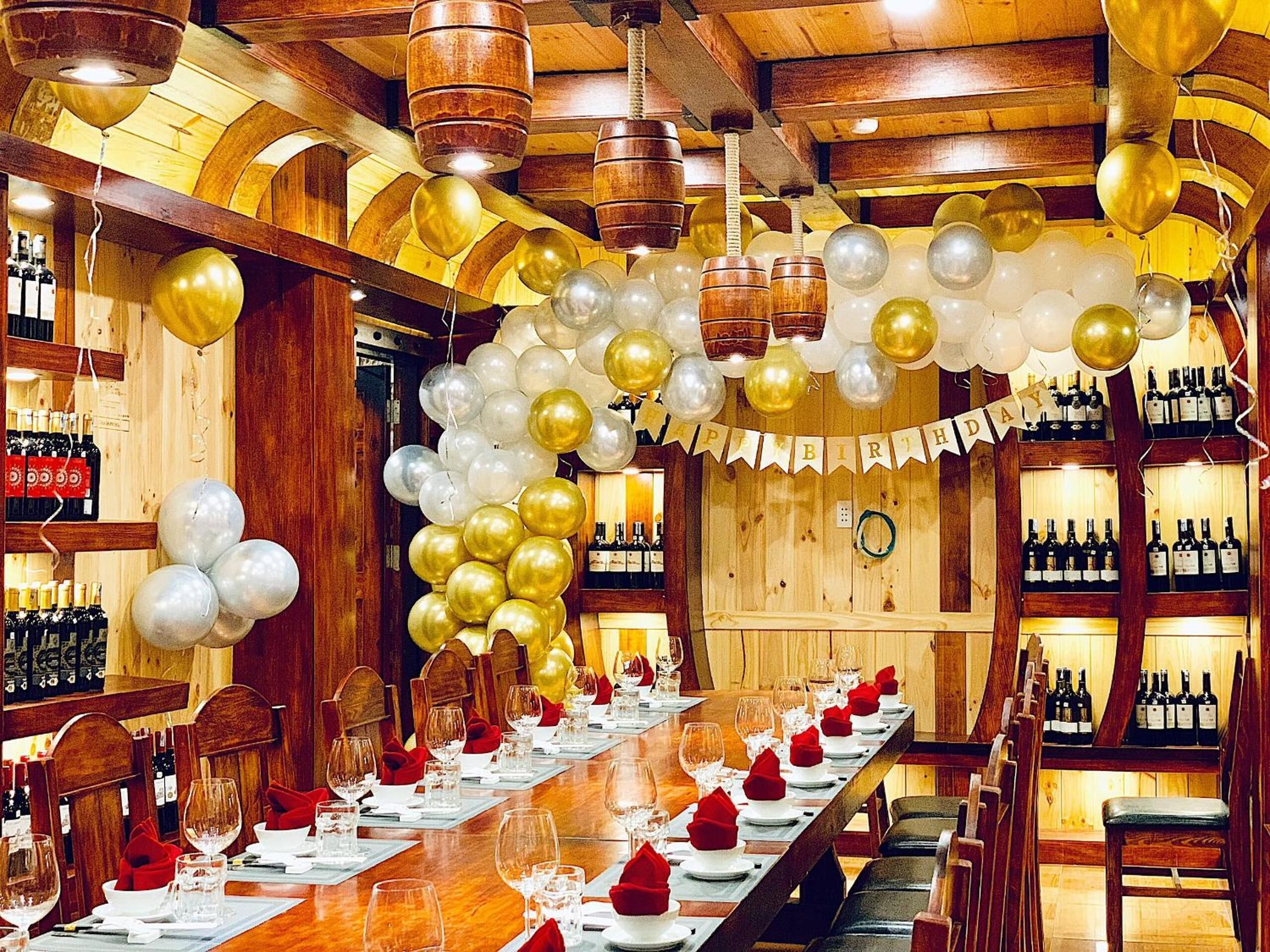 A long dining table set for a celebration with balloons and a banner reading "Happy Birthday".