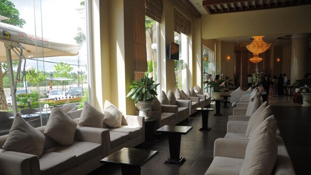A hotel lobby with sofas and tables arranged along a wall with large windows. - Viet Uc Hotel (An Hoi)
