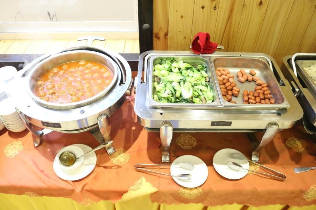 A buffet table with a pot of soup, a tray of vegetables, and a tray of sausages.