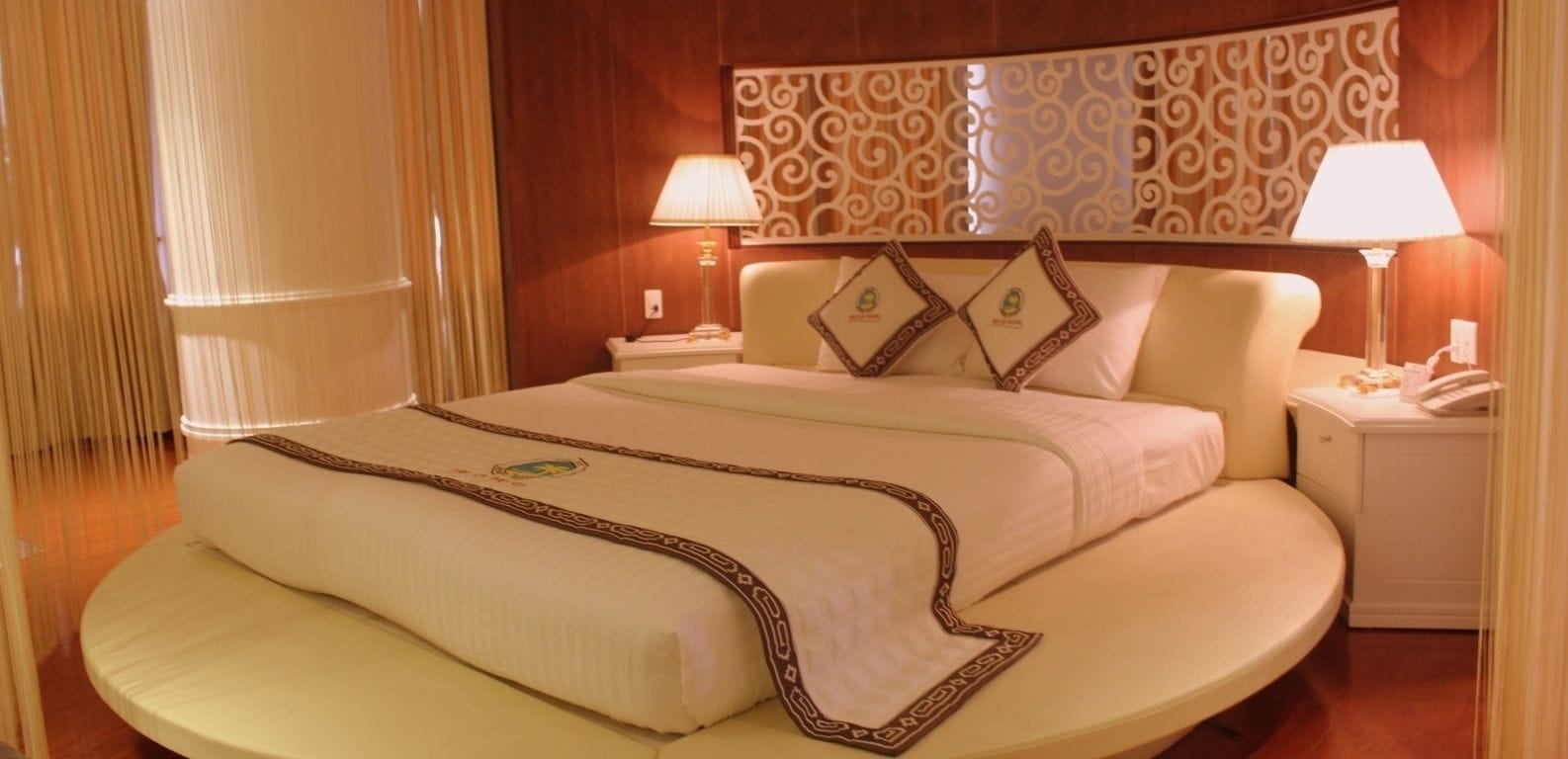 A hotel room with a large bed, two bedside tables, a decorative headboard, and two lamps.