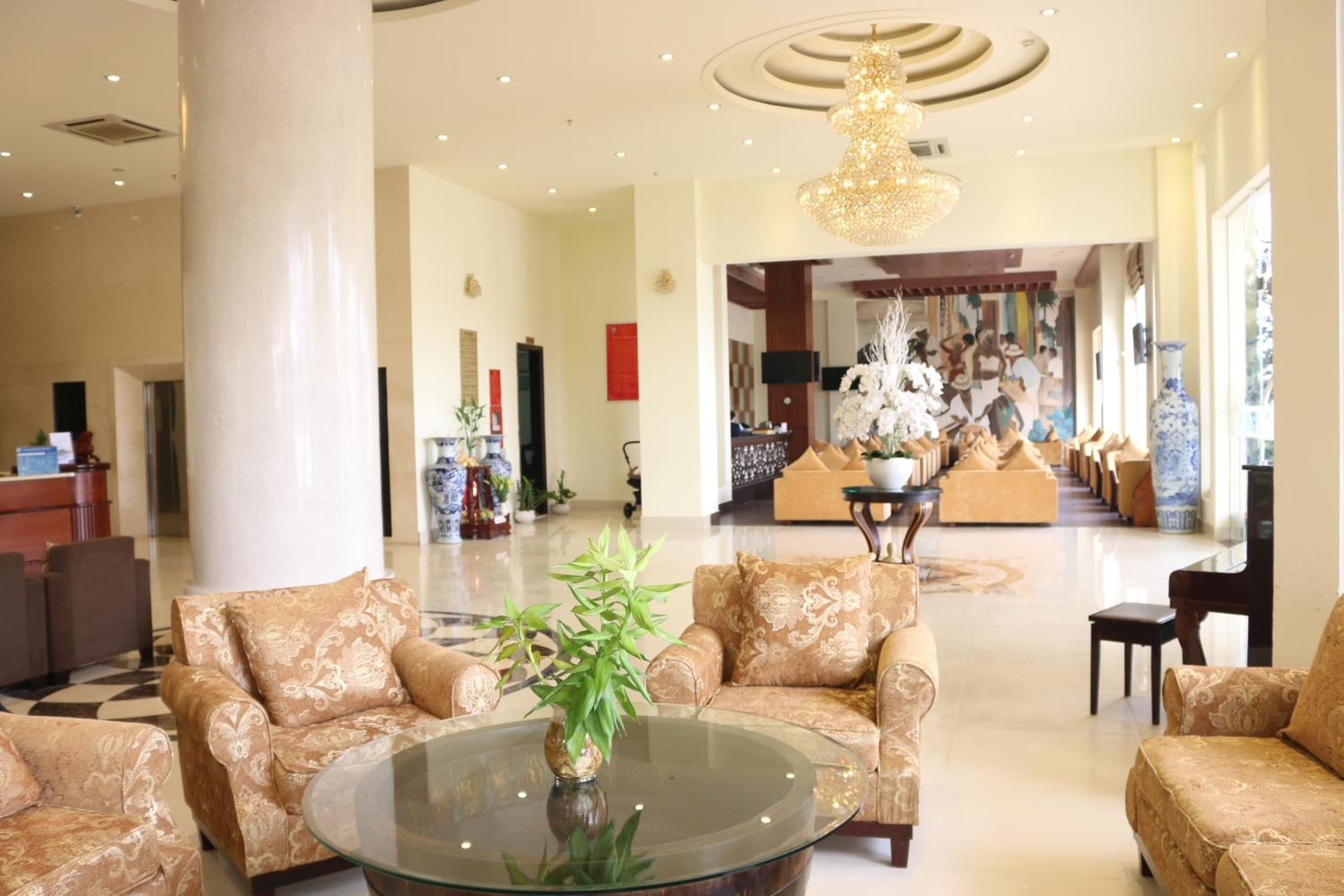 A spacious lobby with a high ceiling, a central chandelier, and a seating area with patterned sofas.