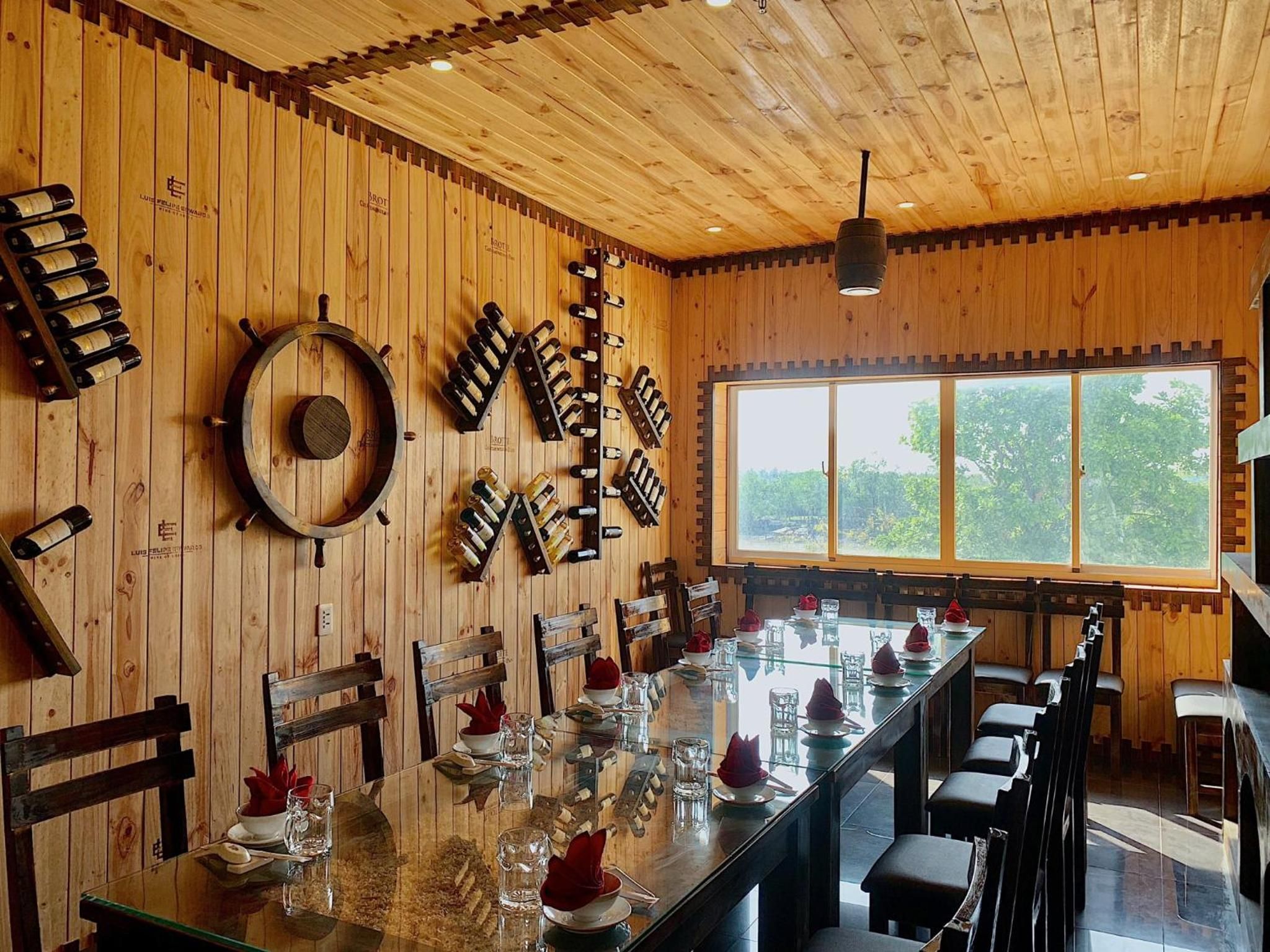 A restaurant with a long wooden table, chairs, and a wine rack on the wall.