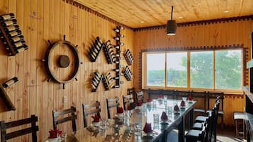 A restaurant with a long wooden table, chairs, and a wine rack on the wall.