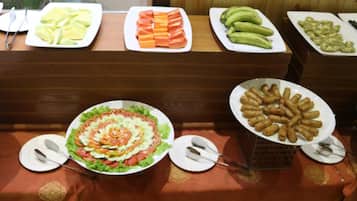 A buffet with various food items including sliced fruits, vegetables, and a salad.