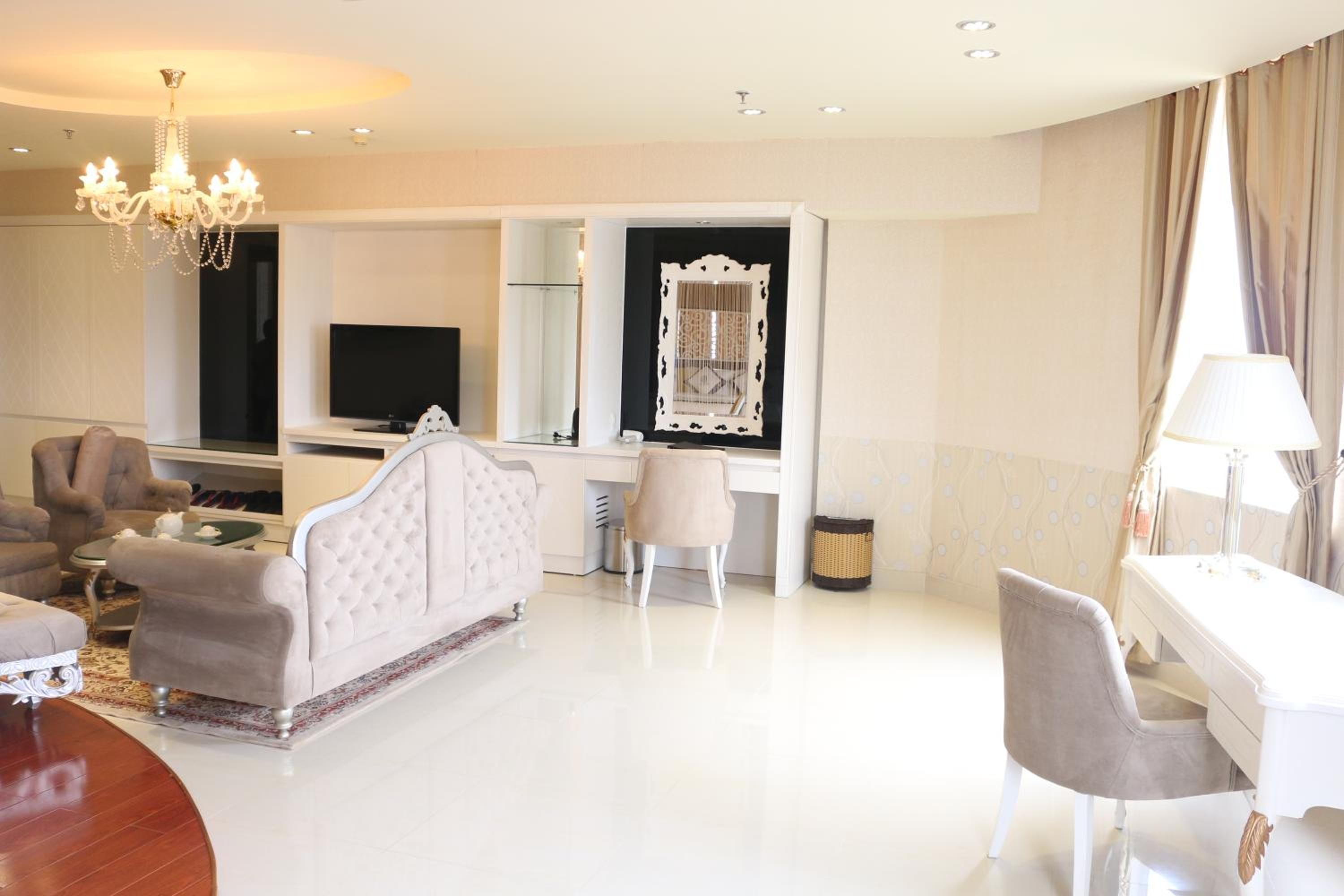 A modern hotel room with a television, a desk, a chair, a sofa, and a chandelier.