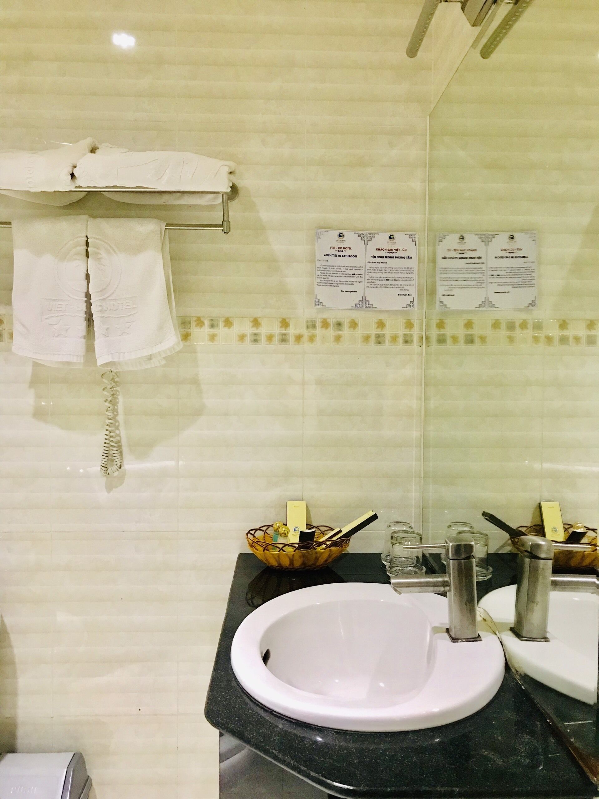 Een badkamer met een wastafel, spiegel en handdoekrek. Er hangen borden aan de muur en er staat een mandje met toiletartikelen.