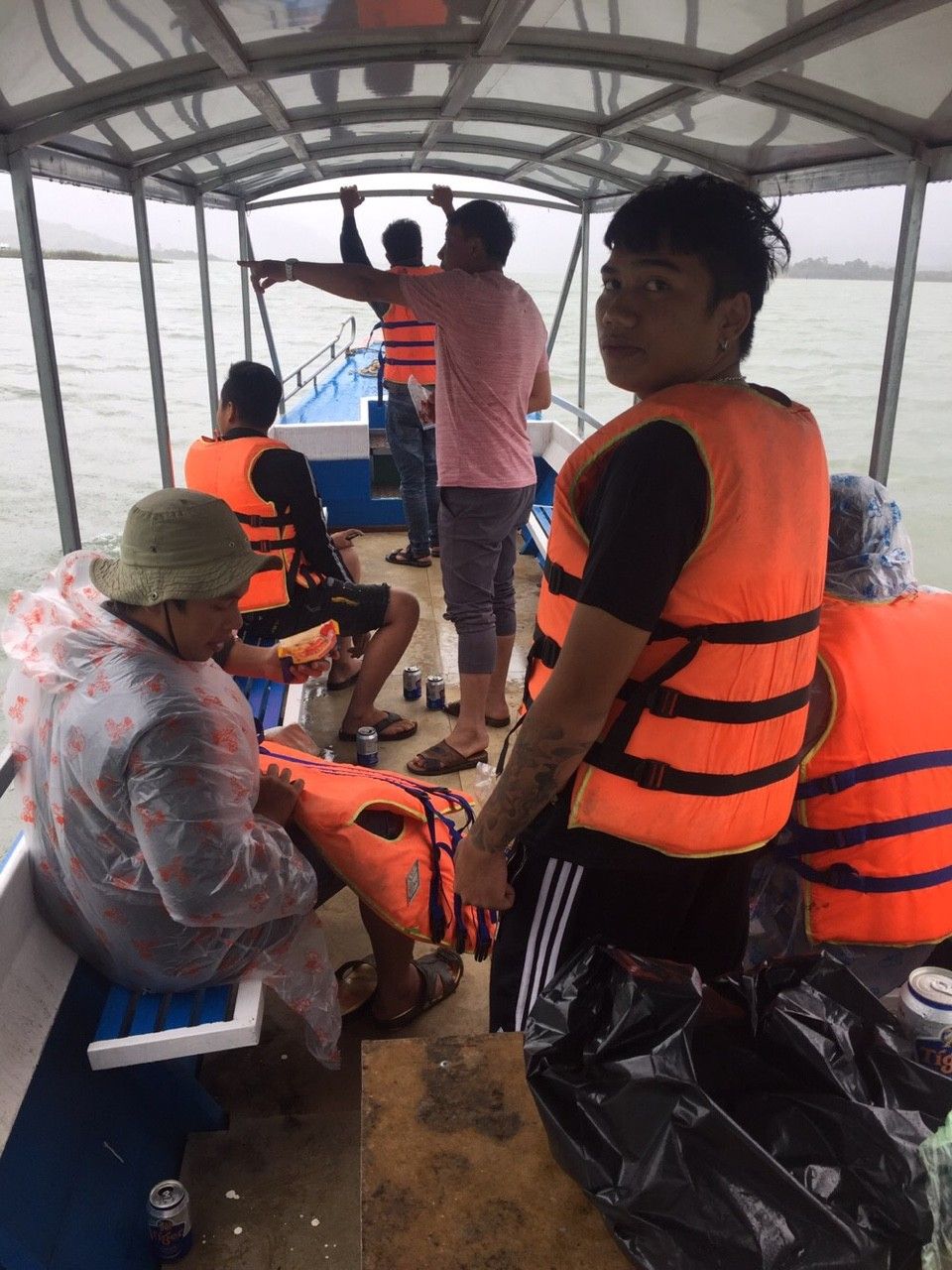 Interior de un barco con personas usando chalecos salvavidas, una zona cubierta y vista al agua.