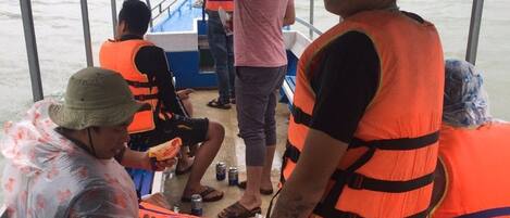 Interior de un barco con personas usando chalecos salvavidas, una zona cubierta y vista al agua.
