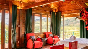 Una cabaña de madera con balcón, sillas rojas, una cama y una mesa.
