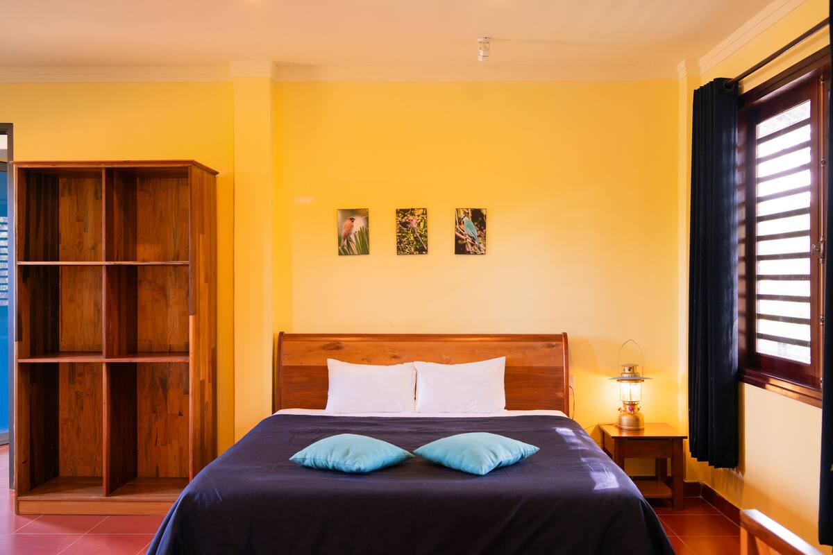 A room with a bed, a wooden wardrobe, and a nightstand with a lamp.