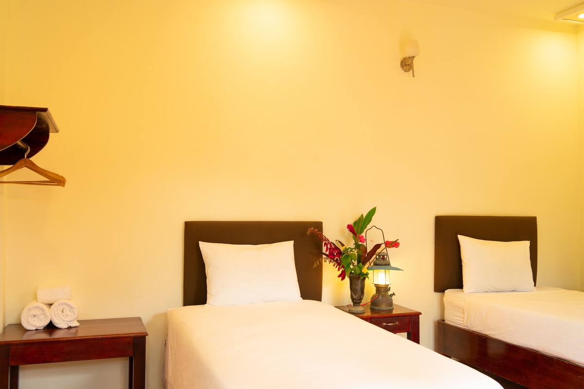 A hotel room with two beds, a nightstand with a lamp, a vase with flowers, and a wooden hanger on the wall.