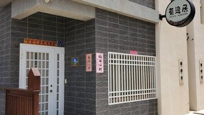Un bâtiment à la structure à deux étages, doté d’une entrée fermée par un portail et d’une enseigne indiquant un commerce nommé « Juviju Honestay ».