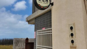 Un bâtiment moderne avec une enseigne indiquant « Jujitsu Homestay » et une entrée fermée par un portail.
