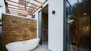 A modern bathroom with a freestanding bathtub, stone wall, and glass shower enclosure. - The Watermark Beachside Hotel (Da Nang)