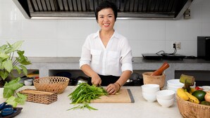 A kitchen with a person chopping vegetables, a wooden cutting board, and various kitchen utensils and containers. - The Watermark Beachside Hotel (Da Nang)