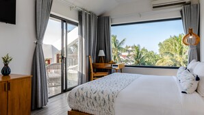 A bedroom with a large bed, a desk, and a view of palm trees. - The Watermark Beachside Hotel (Da Nang)