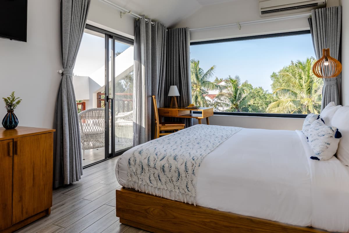 A bedroom with a large bed, a desk, and a view of palm trees.