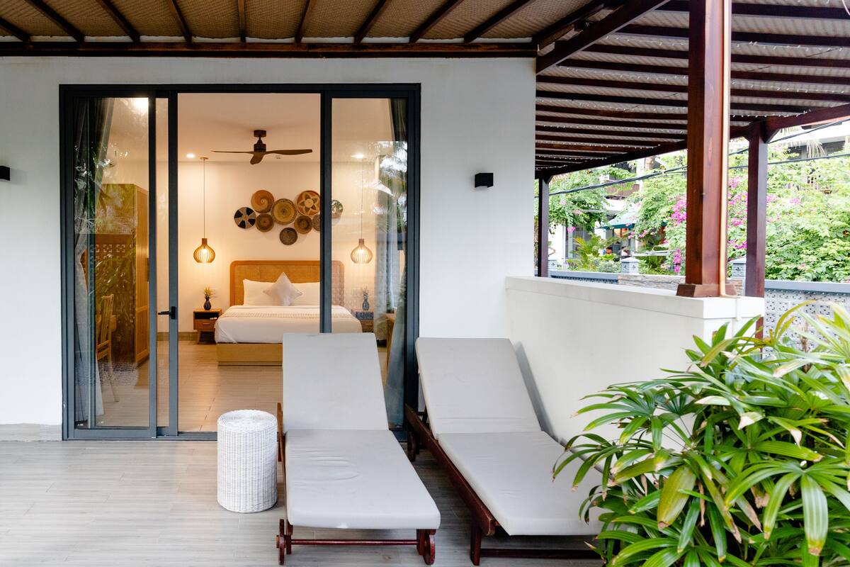 A modern room with a bed, two lounge chairs, a ceiling fan, and a view of greenery outside.