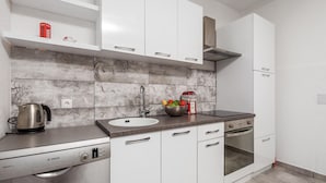 A modern kitchen with white cabinets, a stainless steel Bosch dishwasher, a kettle, and a bowl of fruit on the counter. - Nice apartment in Rijeka (Rijeka)