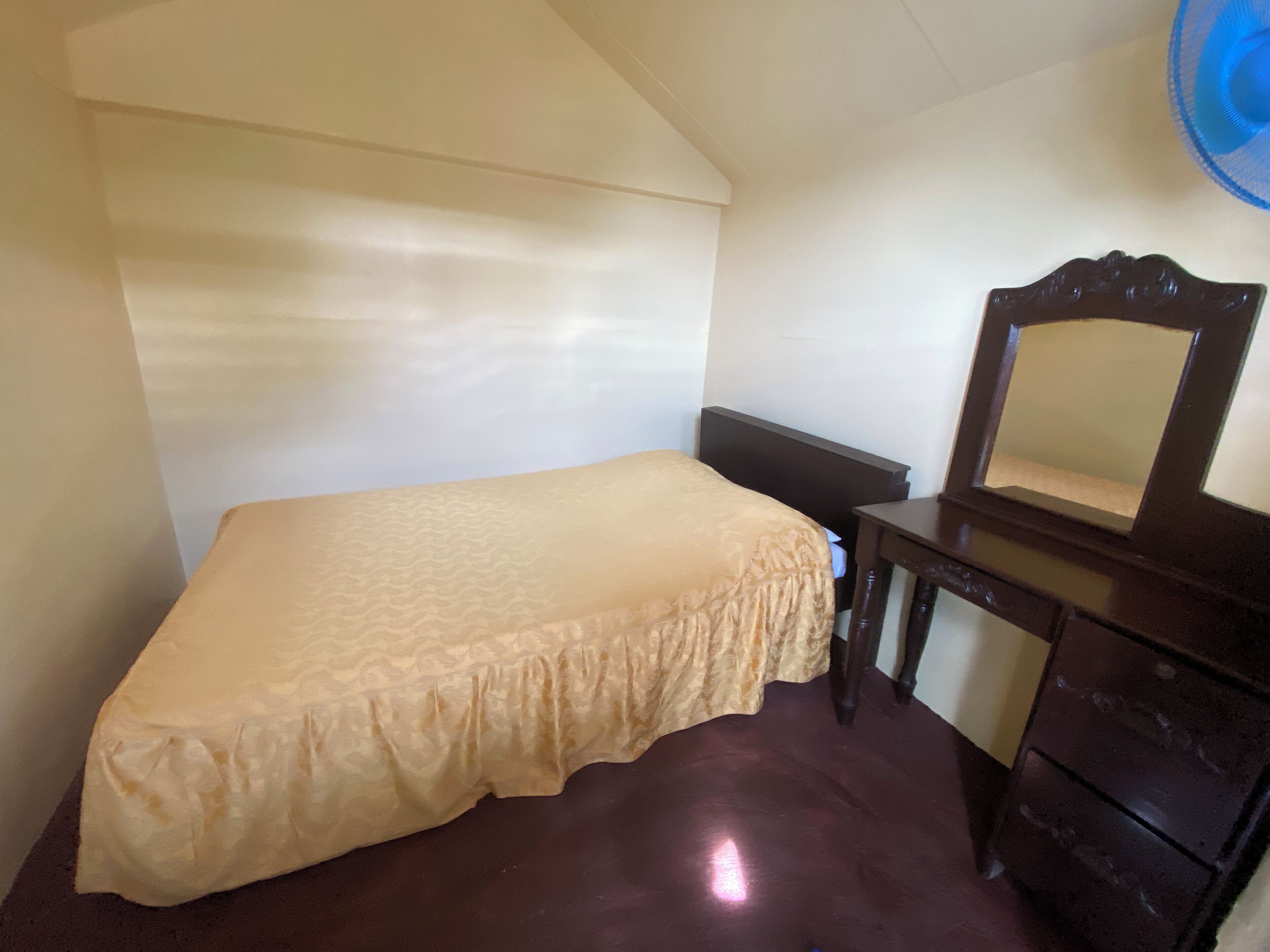 Une petite chambre avec un lit simple, une commode en bois et un miroir.