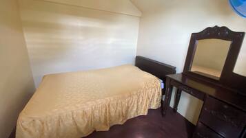 Une petite chambre avec un lit simple, une commode en bois et un miroir.