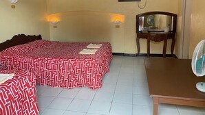 A hotel room with a large bed, a desk, a chair, and a standing fan. - Napo Beach Resort (Maripipi)