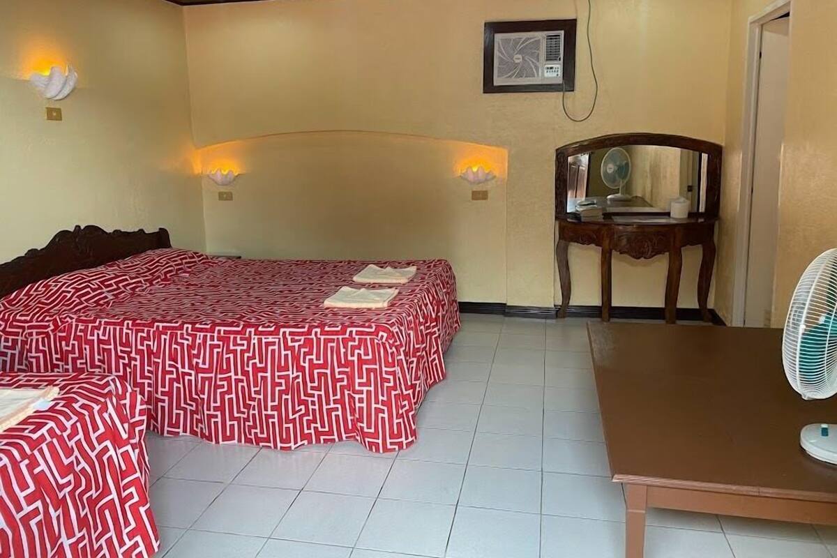Ein Hotelzimmer mit einem großen Bett, einem Schreibtisch, einem Stuhl und einem Standventilator.