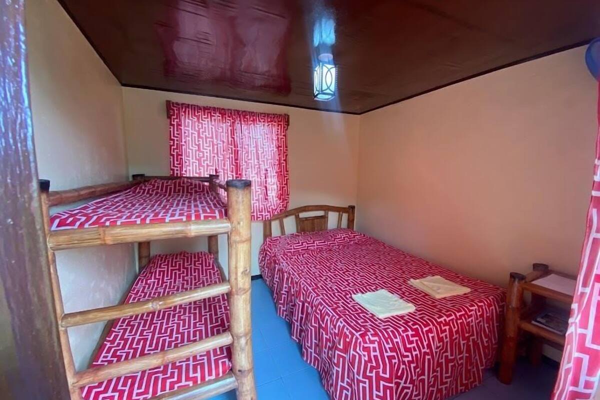Ein Schlafsaalzimmer mit Etagenbetten und einem Einzelbett, Holzmöbeln und einem Fenster mit Vorhängen.