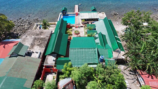 A coastal property with a swimming pool, green-roofed buildings, and a view of the sea. - Napo Beach Resort (Maripipi)