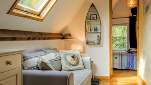 A cozy room with a loft bed, a wooden beam ceiling, a small shelf with decorative items, and a view of the outdoors through a window.