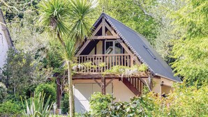 A wooden house with a balcony, surrounded by lush greenery.
