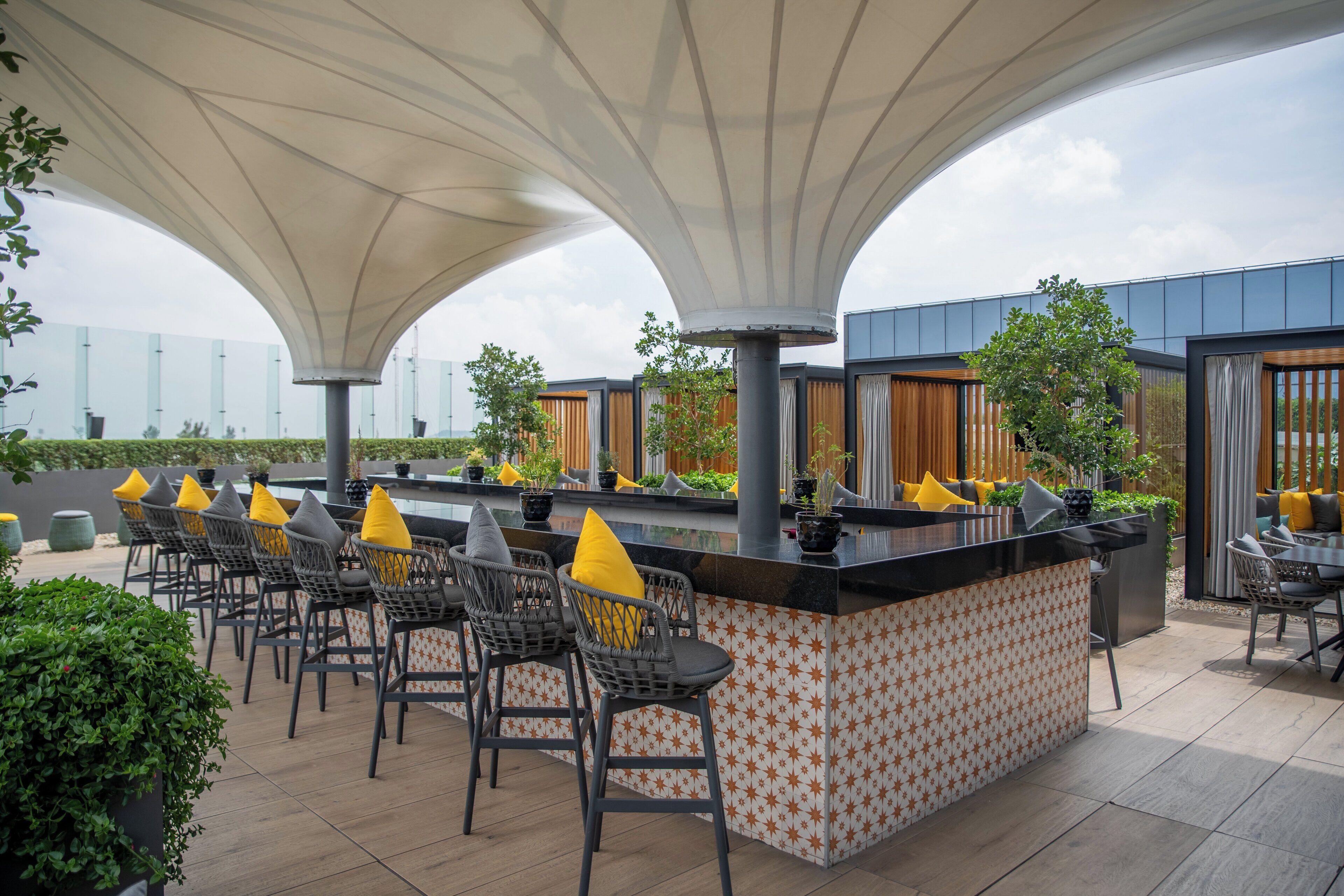 An outdoor bar area with a patterned bar counter, multiple seating arrangements, and a canopy overhead.