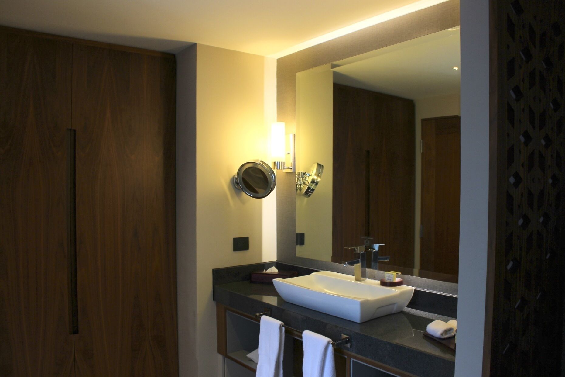 A modern bathroom with a large mirror, a white sink, and wooden cabinets.