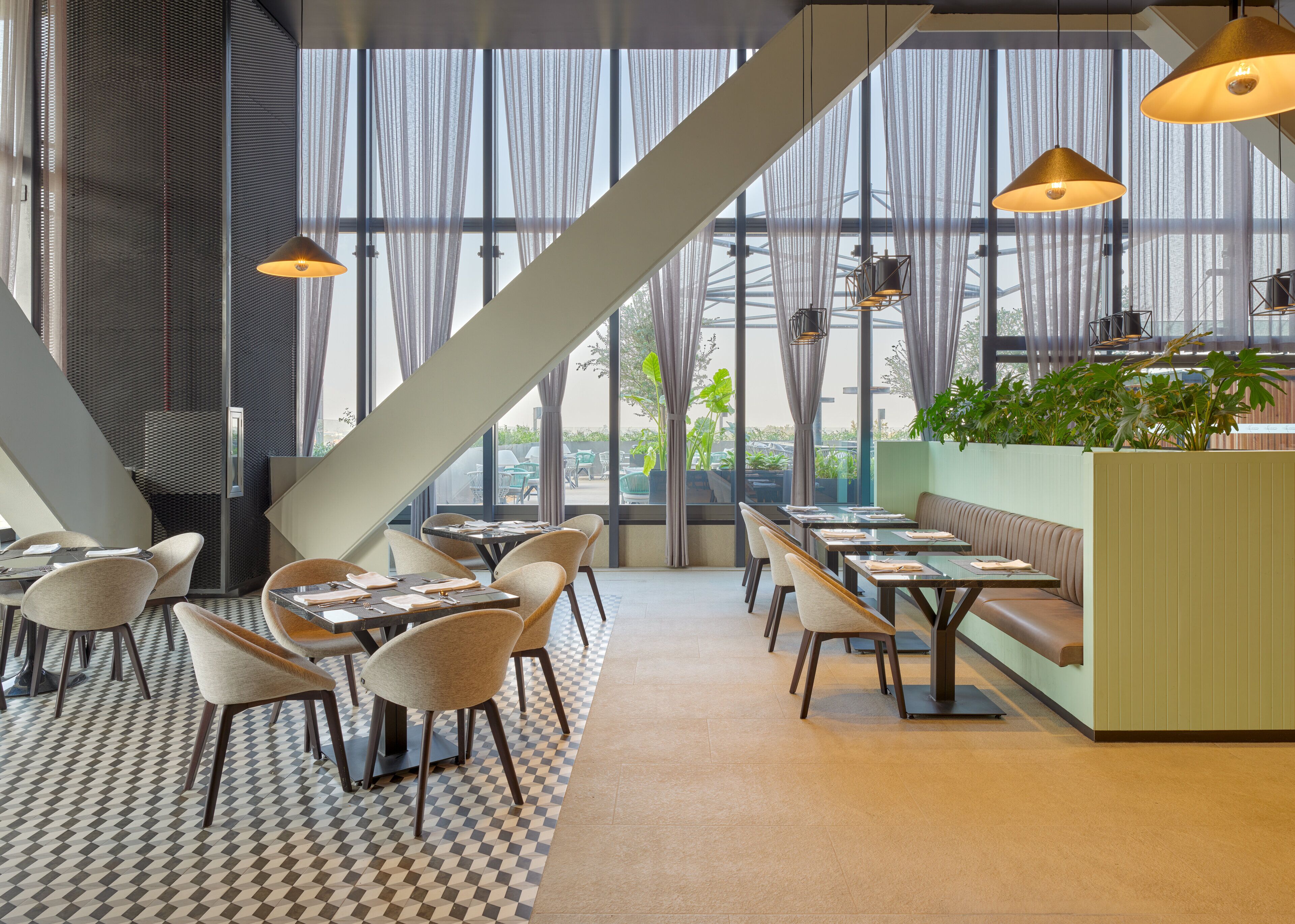 Un restaurante moderno con suelo de cuadros, ventanas amplias y una variedad de asientos, incluyendo mesas y una cabina.