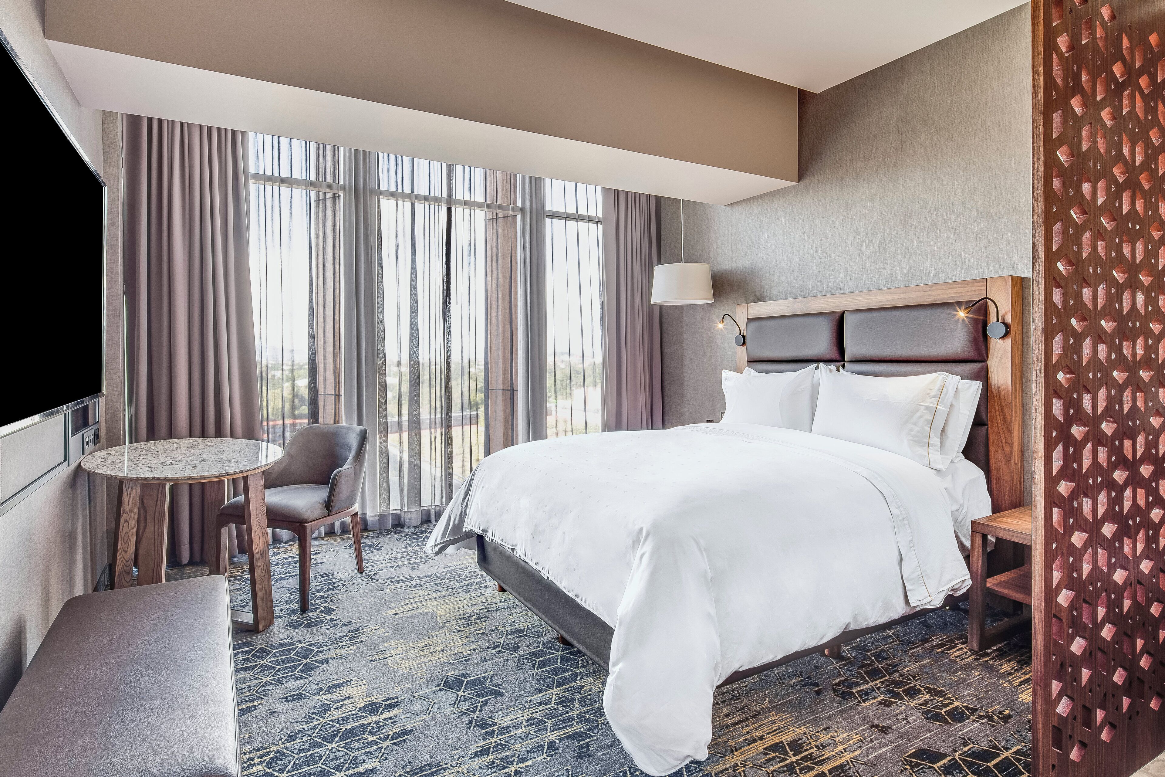 A hotel room with a large bed, a round table, a chair, and a TV.