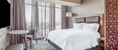 A hotel room with a large bed, a round table, a chair, and a TV.