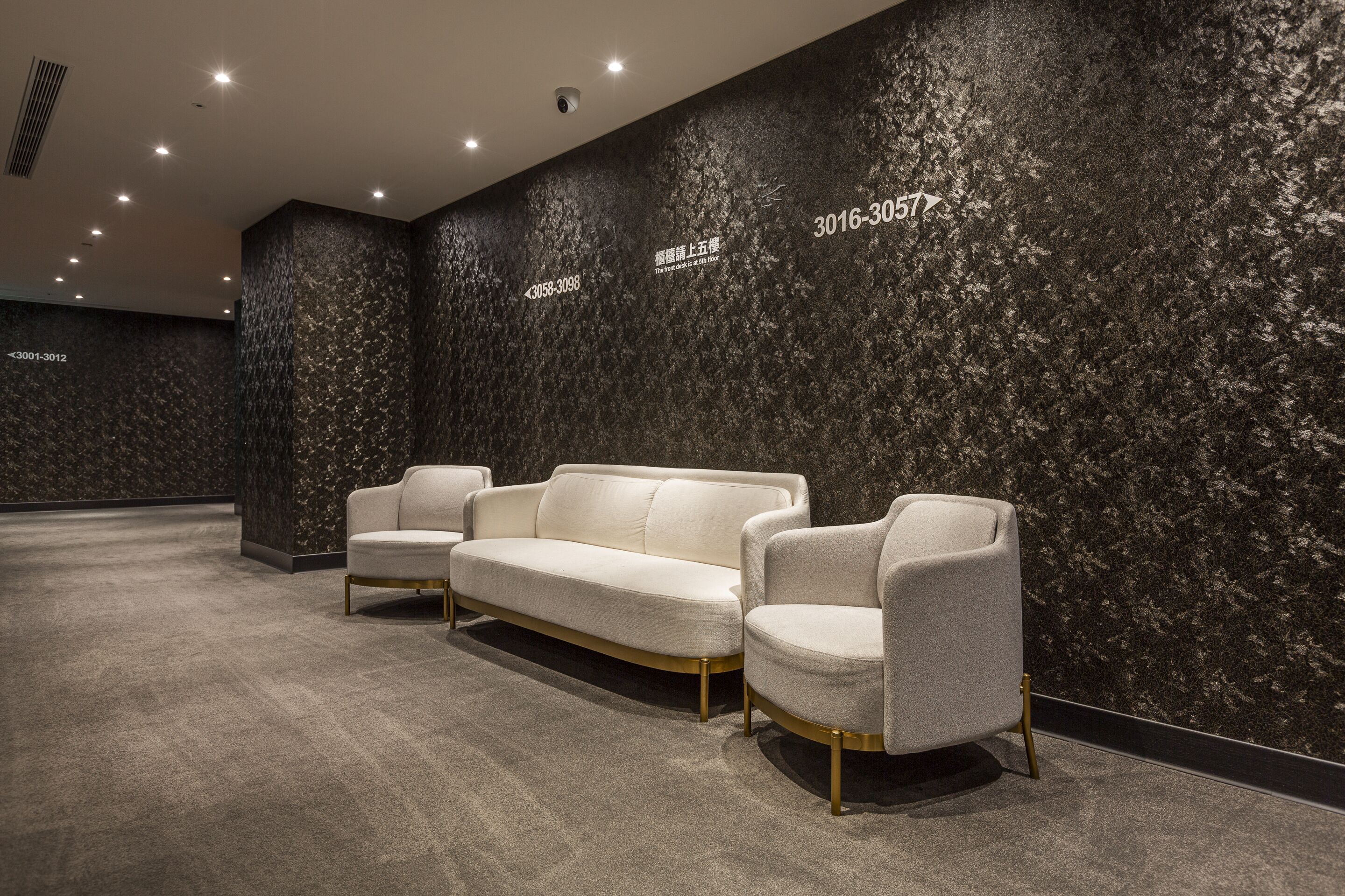 A modern lobby with a dark textured wall, a white sofa, and two armchairs.