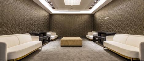 A modern, well-lit room with a high ceiling, a central ottoman, and two sofas.