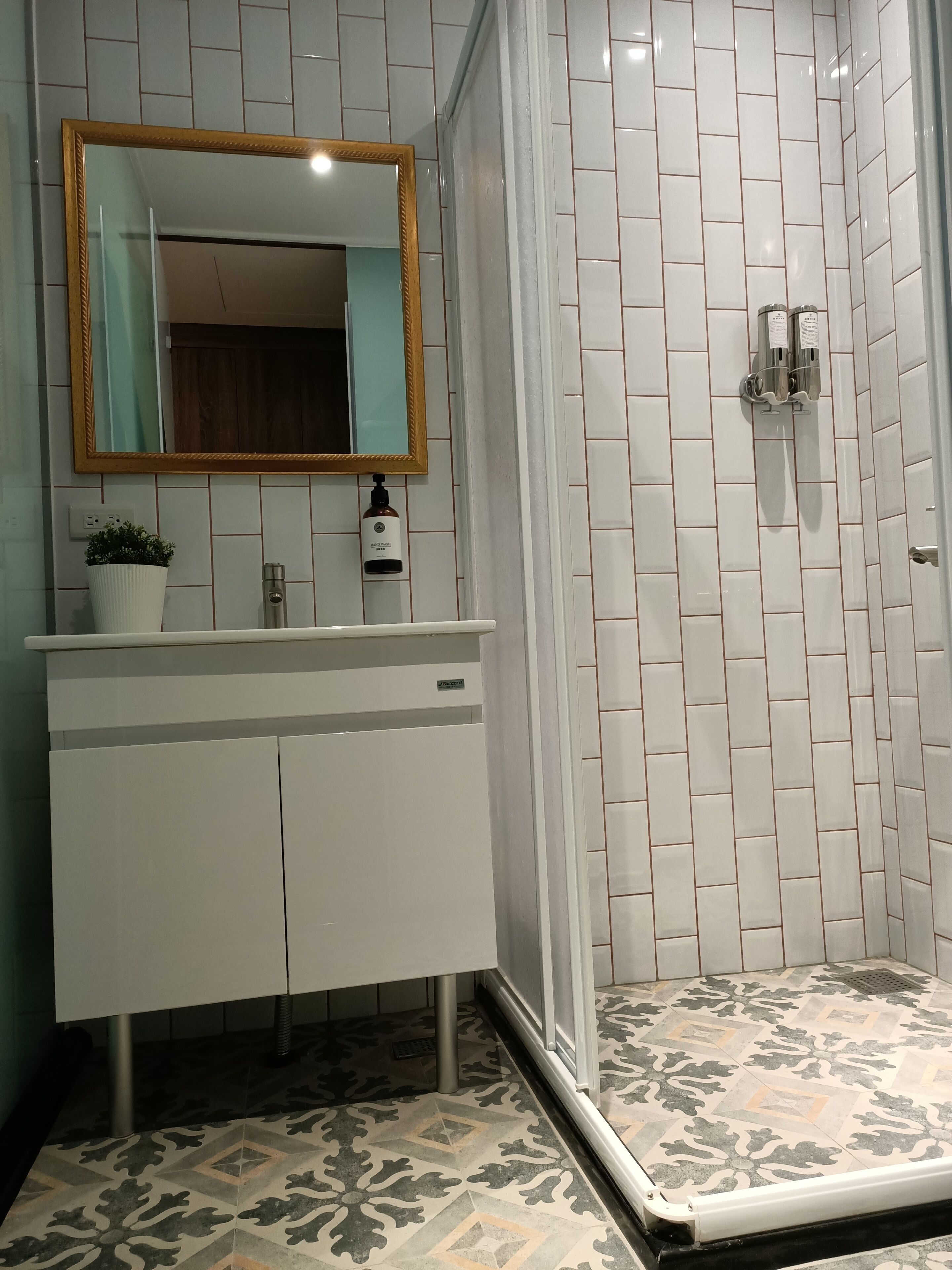 A bathroom with a white vanity, a mirror, a shower with white tiles, and patterned floor tiles.