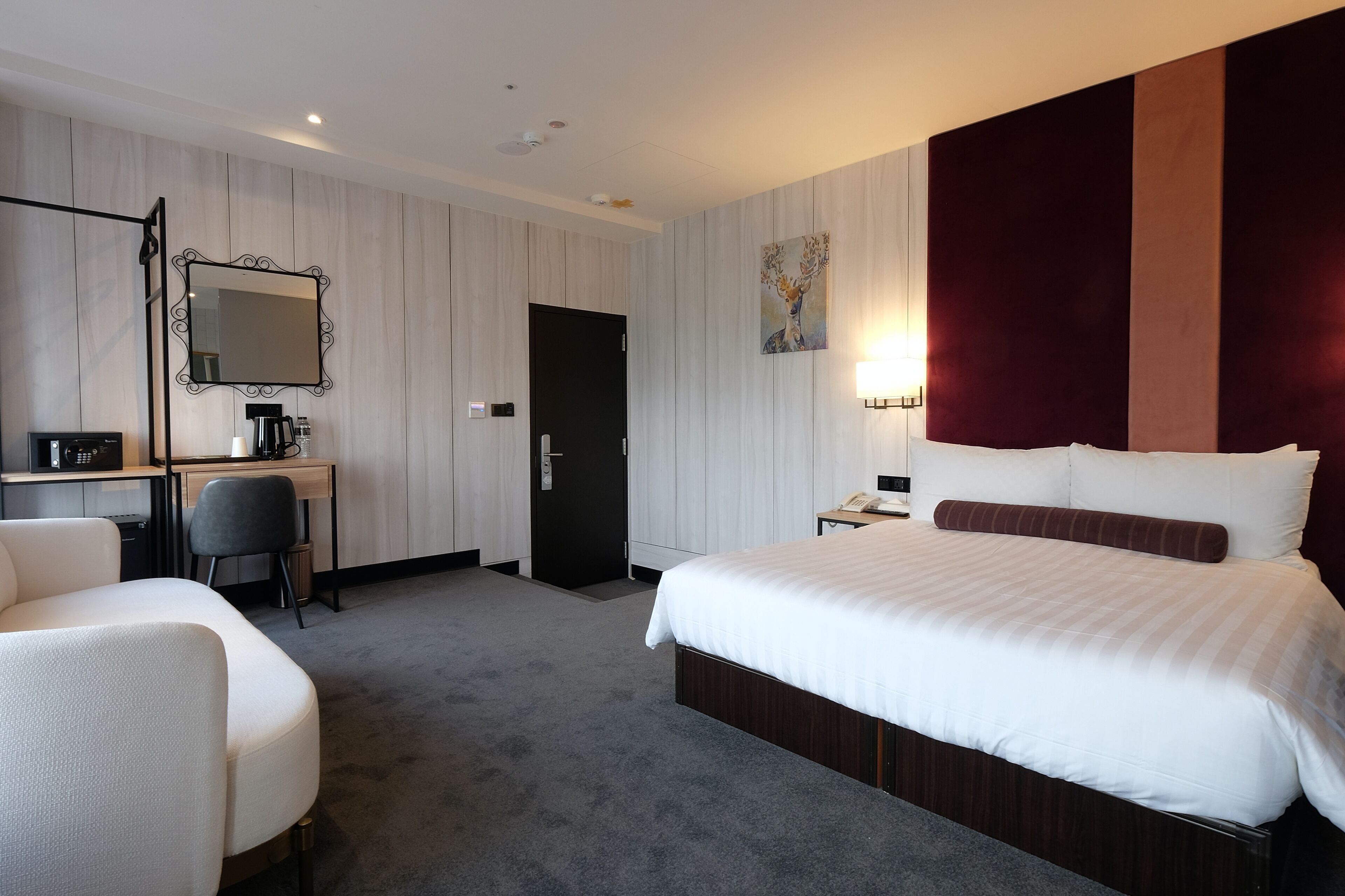 A hotel room with a large bed, a desk with a chair, a mirror, and a painting on the wall.