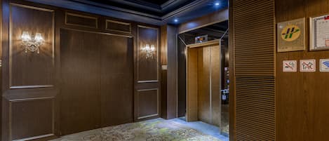 Un pasillo con paneles de madera, alfombra estampada y una lámpara fijada a la pared.