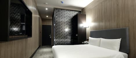 Una habitación de hotel con una cama grande, un televisor en la pared izquierda y una puerta que da a otra habitación.